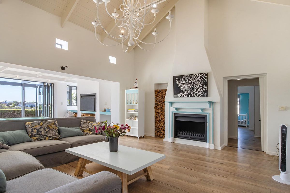 Spacious living room featuring a vaulted ceiling with exposed beams, a fireplace with a mantelpiece, timber flooring, and bi-fold doors leading to the outdoors.