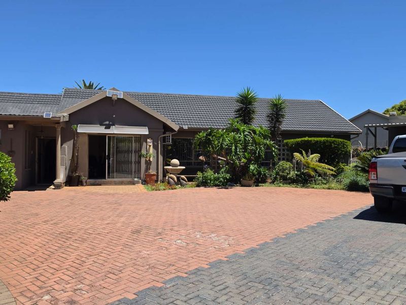 Front exterior view of a single-story house featuring a large paved driveway, tiled roof, and established garden landscaping.