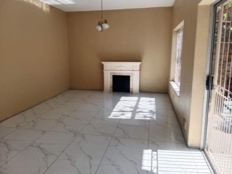 An empty living room featuring marble-look floor tiles, a central fireplace, and a sliding glass door with security gate leading to the exterior.