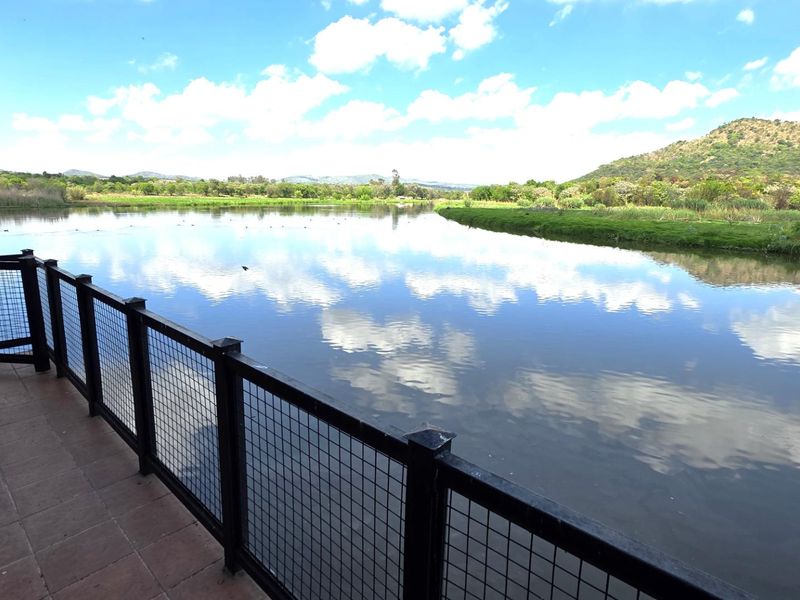 A scenic view of a tranquil river and surrounding landscape, captured from a tiled patio with a secure metal mesh railing.