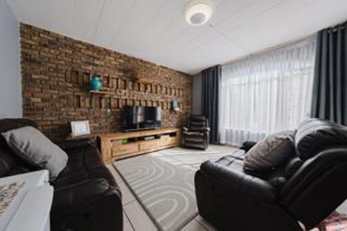 A comfortable living room featuring a prominent exposed brick feature wall, tiled flooring, and large windows allowing for natural light.