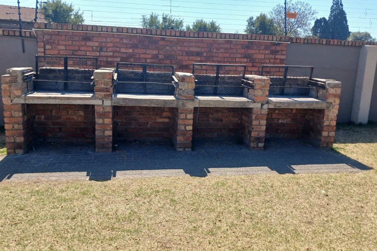 A communal outdoor area featuring a large, multi-section built-in brick braai facility set against a perimeter wall.