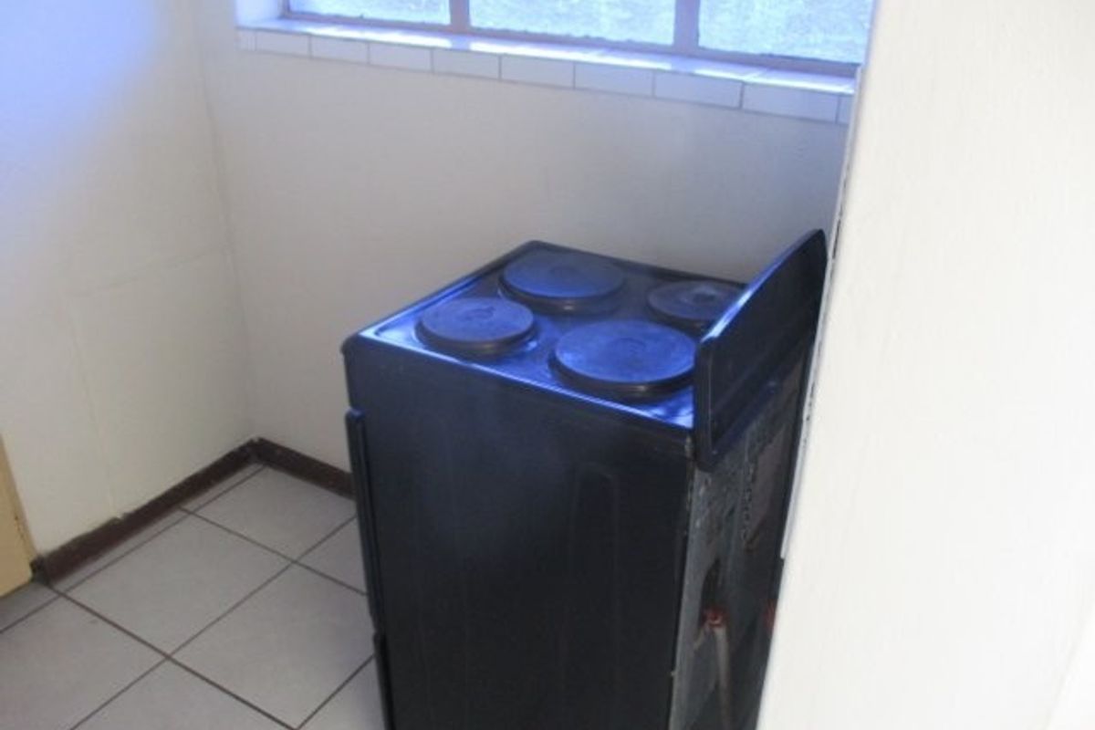 A small kitchen area featuring tiled flooring and a standalone electric stove positioned beneath a window.
