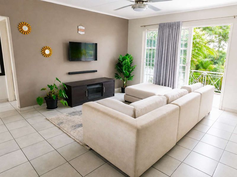 A bright living room featuring tiled flooring, a ceiling fan, and a sliding glass door providing access to a balcony.
