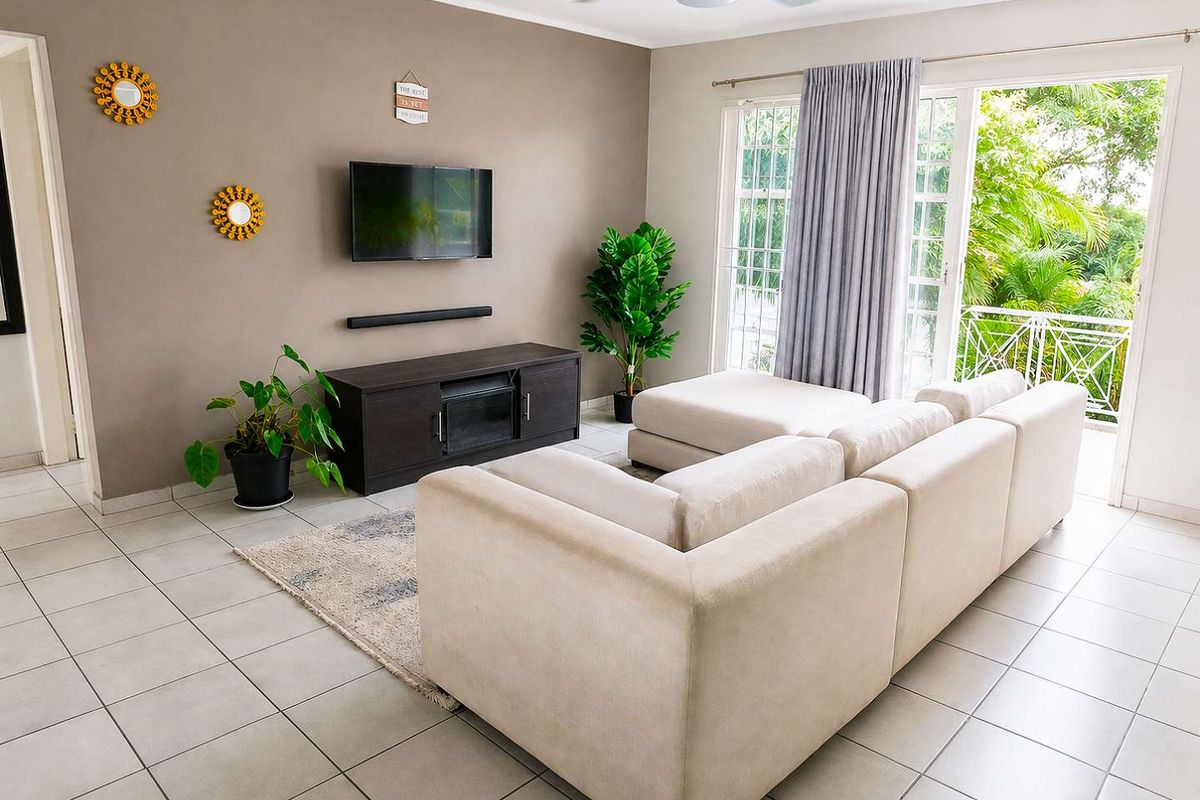 A bright living room featuring tiled flooring, a ceiling fan, and a sliding glass door providing access to a balcony.