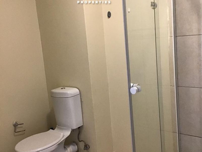 A functional bathroom featuring a standard toilet and a glass-enclosed shower with tiled finishes.