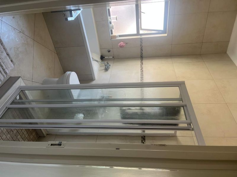 A functional bathroom featuring a built-in bathtub, a separate shower enclosure with a folding door, and neutral wall and floor tiling.