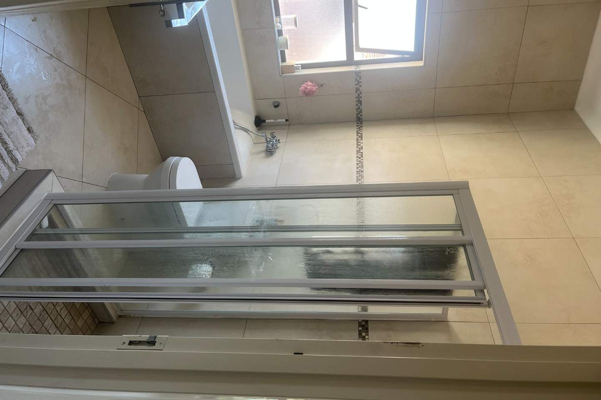 A functional bathroom featuring a built-in bathtub, a separate shower enclosure with a folding door, and neutral wall and floor tiling.