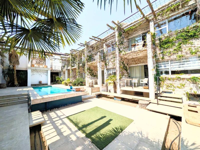 A multi-level guest house courtyard featuring a swimming pool, concrete patio areas, and balconies with climbing vegetation on the building facade.