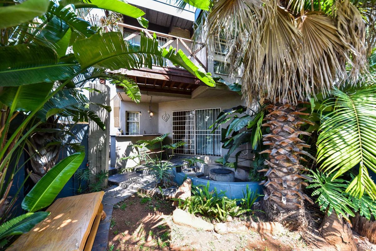 Rear exterior view of the townhouse featuring a wooden balcony, sliding door access, and a built-in bar area set within a lush garden.