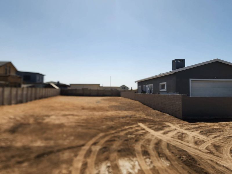 A spacious vacant residential plot featuring a perimeter boundary wall and an adjacent garage structure with a chimney.