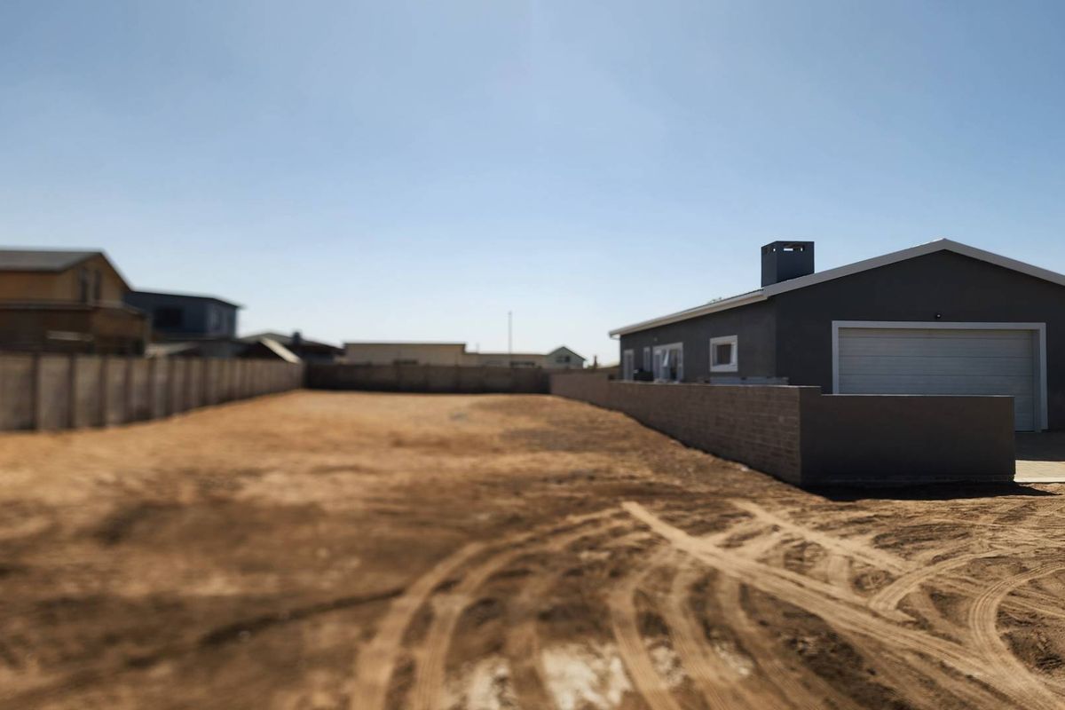 A spacious vacant residential plot featuring a perimeter boundary wall and an adjacent garage structure with a chimney.