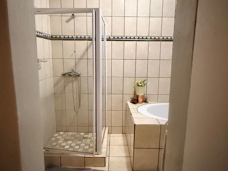 A functional bathroom featuring a tiled shower enclosure and a built-in bathtub with neutral ceramic wall and floor tiling.