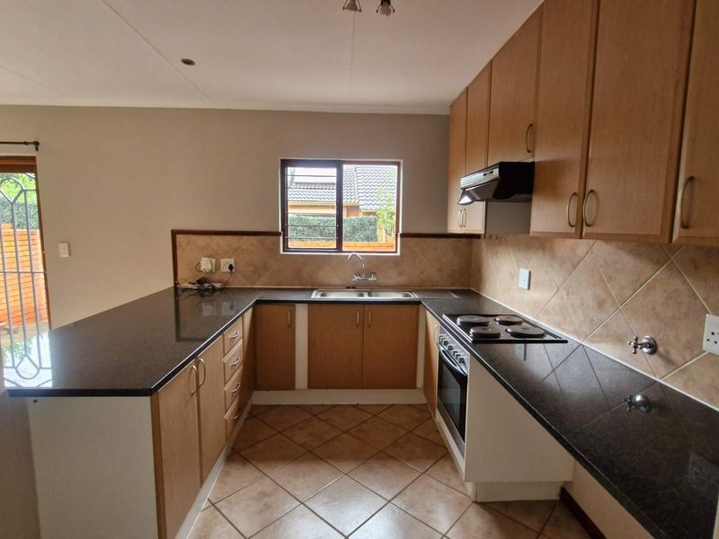 A functional kitchen featuring granite countertops, wooden cabinetry, built-in oven, electric hob, and tiled flooring, offering a clean and practical workspace.