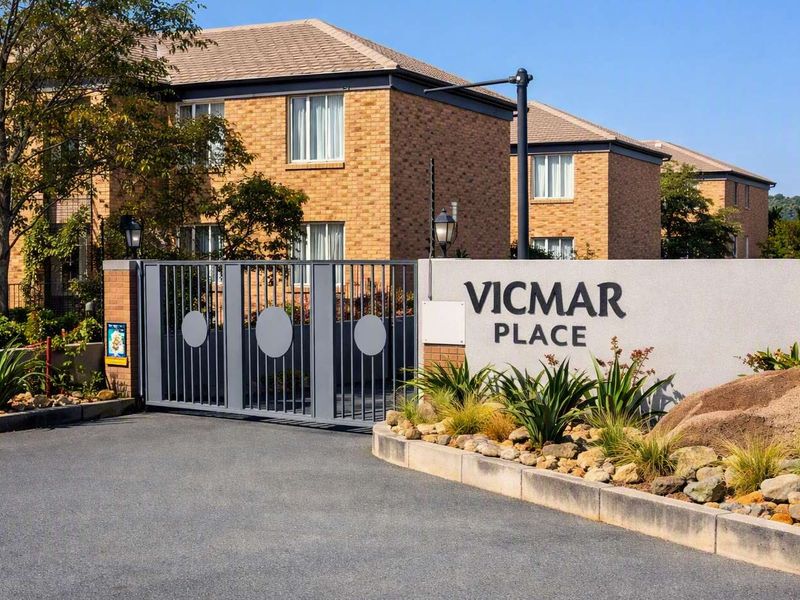 The entrance to Vicmar Place townhouse complex, featuring a secure gated access, brick facade buildings, and well-maintained landscaped garden areas.