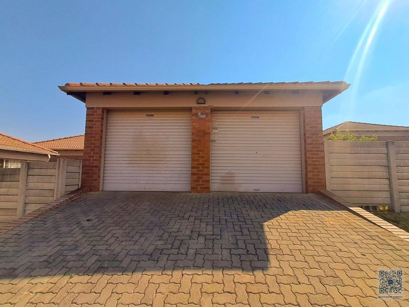 A double garage featuring roller doors, a brick facade, and a paved driveway, set within a secure residential property boundary.