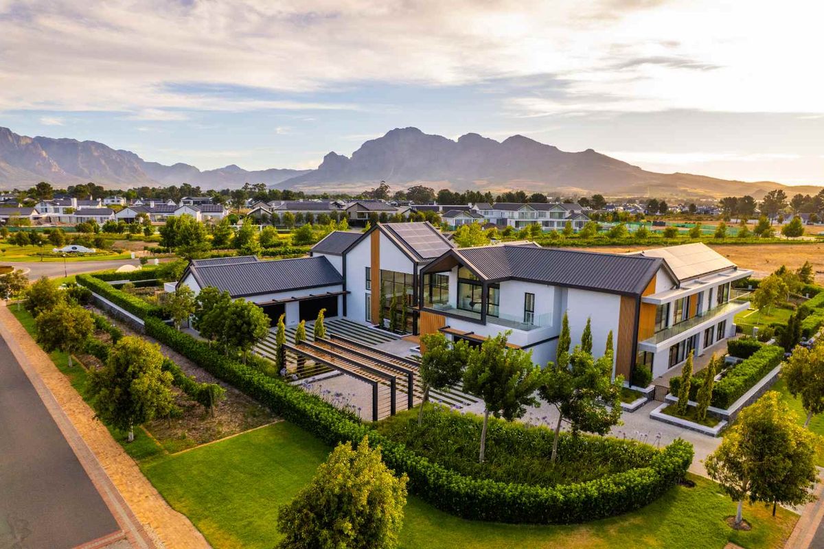 Stunning aerial view of a modern luxury residence featuring solar panels, a landscaped garden, and a pergola, set against a scenic mountain backdrop.