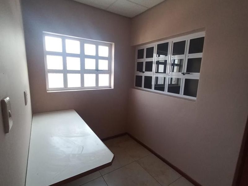 A small, empty office space featuring tiled flooring, a built-in desk, and grid-style windows providing natural light.