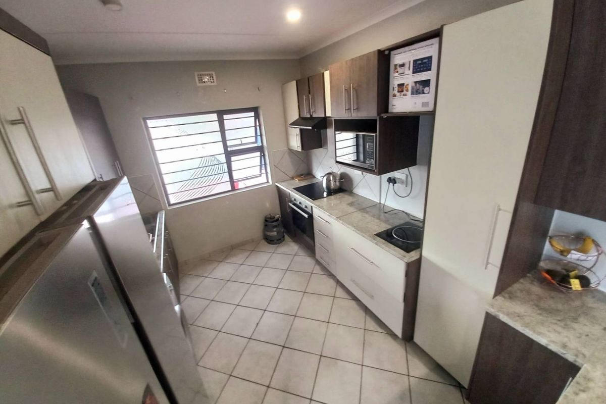 A functional kitchen featuring modern two-tone cabinetry, stone-look countertops, a built-in oven, hob, and tiled flooring with ample natural light.