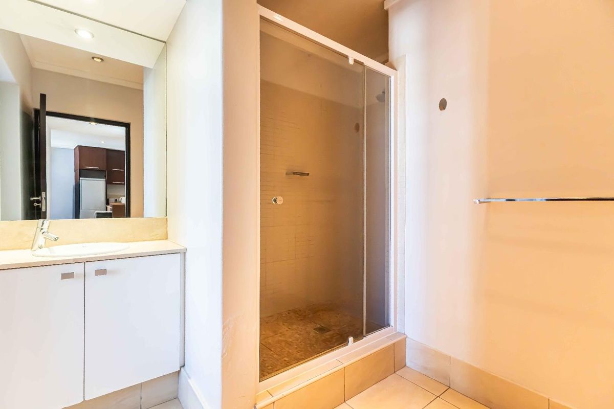 A functional bathroom featuring a vanity with integrated basin, wall mirror, and a glass-enclosed shower with tiled flooring.