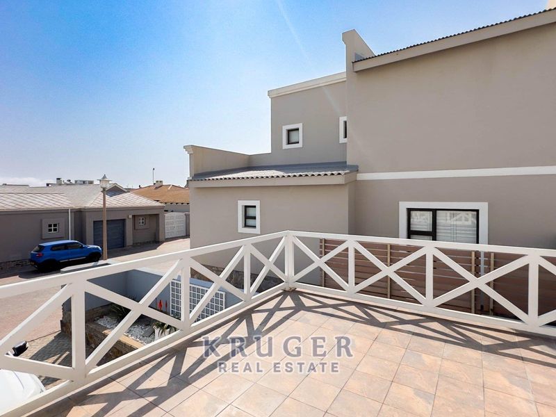 An elevated balcony featuring tiled flooring and a white wooden balustrade, offering an open outdoor space with views of the surrounding residential area.