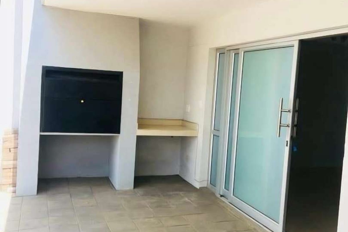 Covered patio area featuring a built-in braai, tiled flooring, and sliding glass doors providing access to the interior living space.