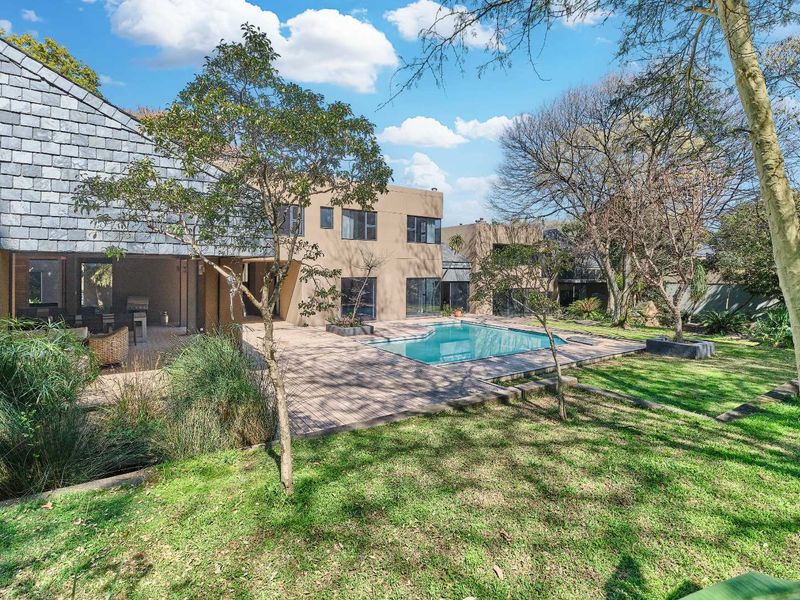 Rear view of the property featuring a swimming pool, paved patio area, and established garden with mature trees.