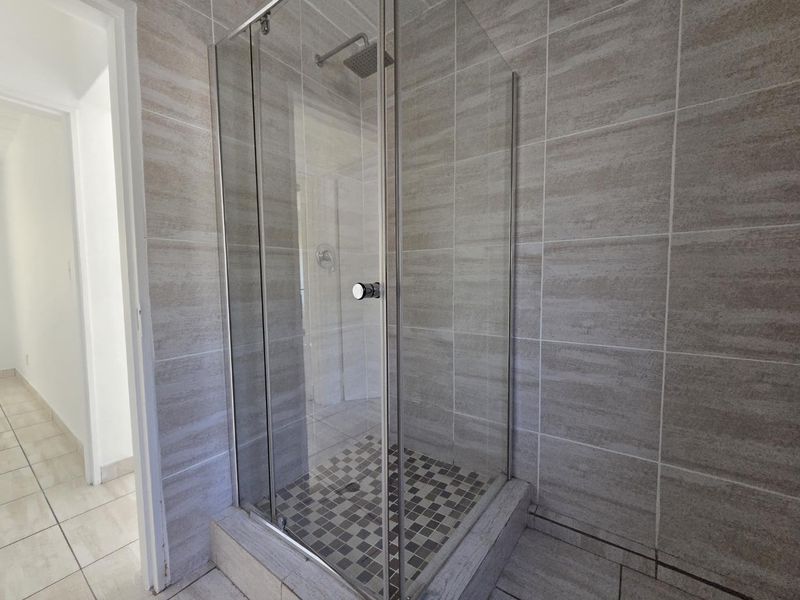 A modern bathroom featuring a glass-enclosed shower with neutral wall tiling and a mosaic-tiled shower floor.