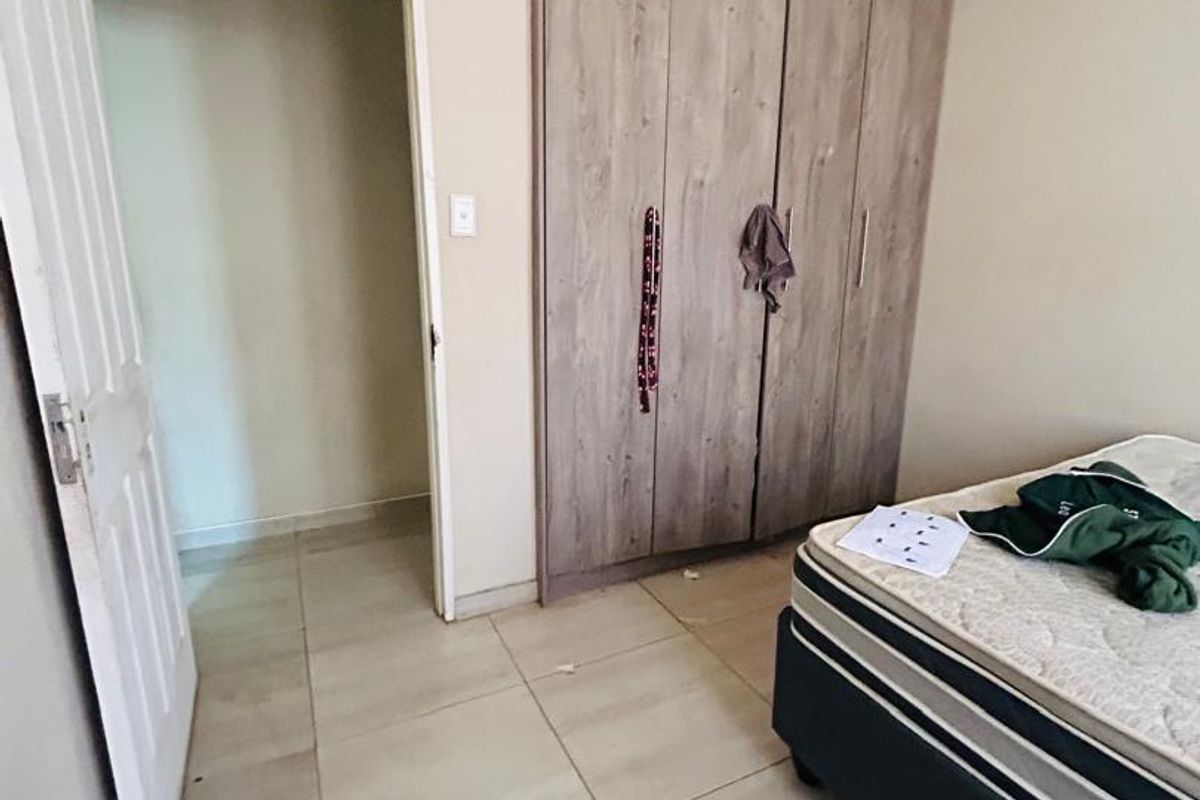 A bedroom featuring built-in wooden cupboards, neutral wall paint, and tiled flooring, with an adjacent doorway leading to an additional space.