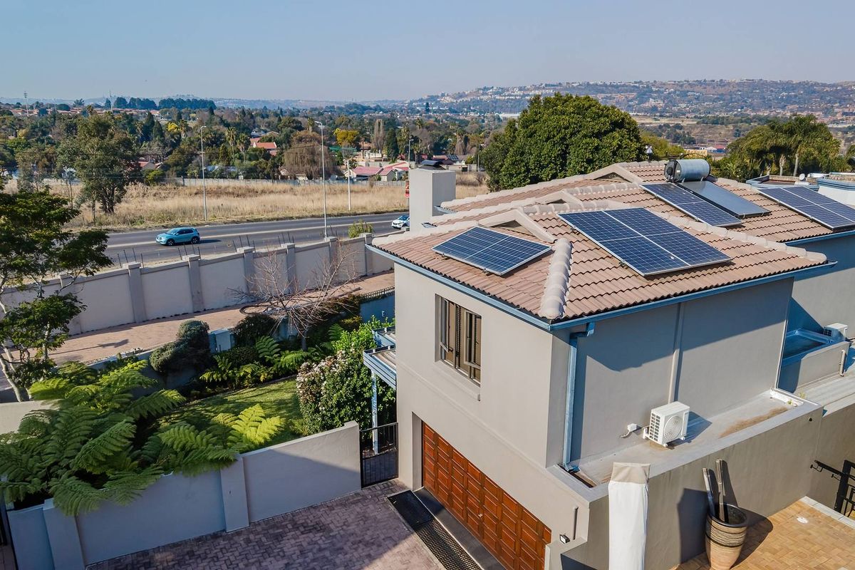 Aerial view of a residential property featuring a tiled roof with solar panels, a solar geyser, a paved driveway, and a secure perimeter wall.