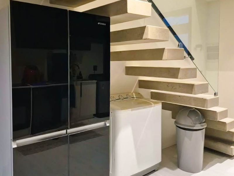 A modern laundry area situated beneath a contemporary floating staircase with a glass balustrade and clean tiled flooring.