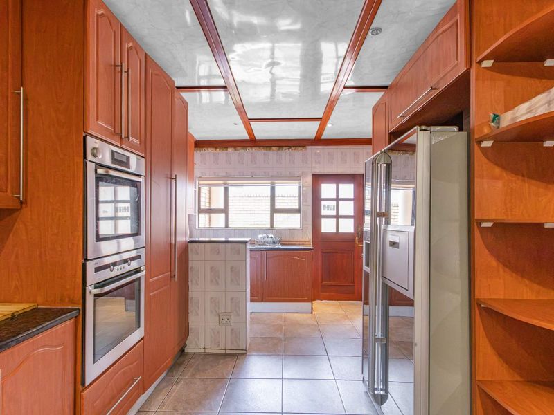 A functional kitchen featuring extensive timber cabinetry, a double wall oven, granite countertops, and tiled flooring with direct access to the exterior.