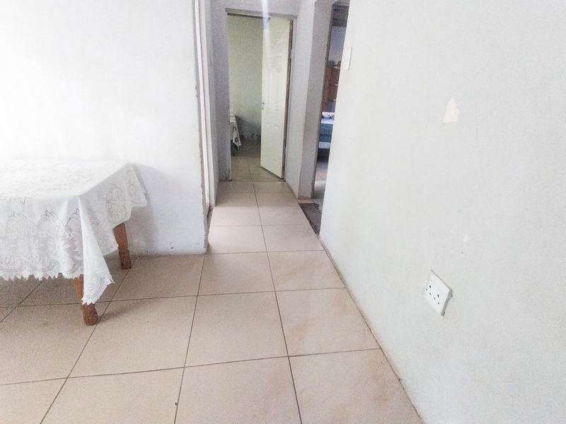 A simple hallway featuring tiled flooring and access to adjacent rooms, showing signs of wear on the wall surfaces.