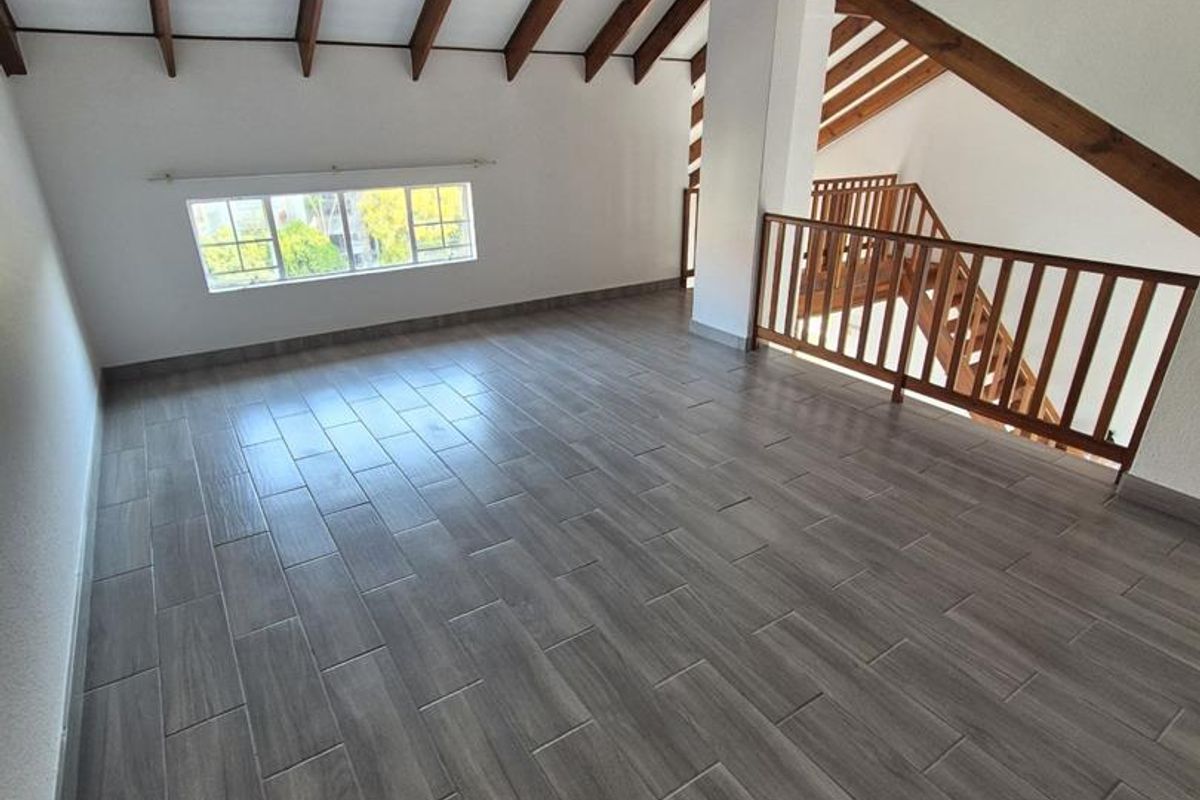 Spacious open-plan living area featuring vaulted ceilings with exposed timber beams, modern tiled flooring, and a wooden staircase railing.
