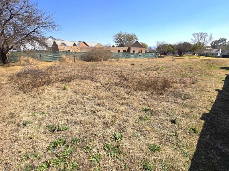 A vacant residential plot featuring a perimeter brick wall and white post and rail fencing, ready for development.