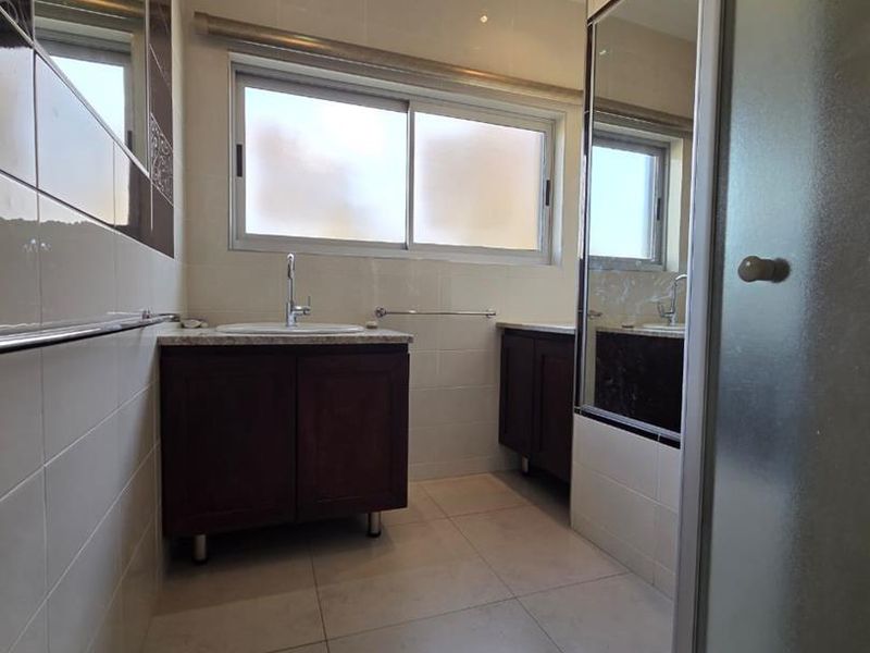 A clean, well-maintained bathroom featuring a vanity cabinet with basin, tiled walls and floors, and a separate shower enclosure.
