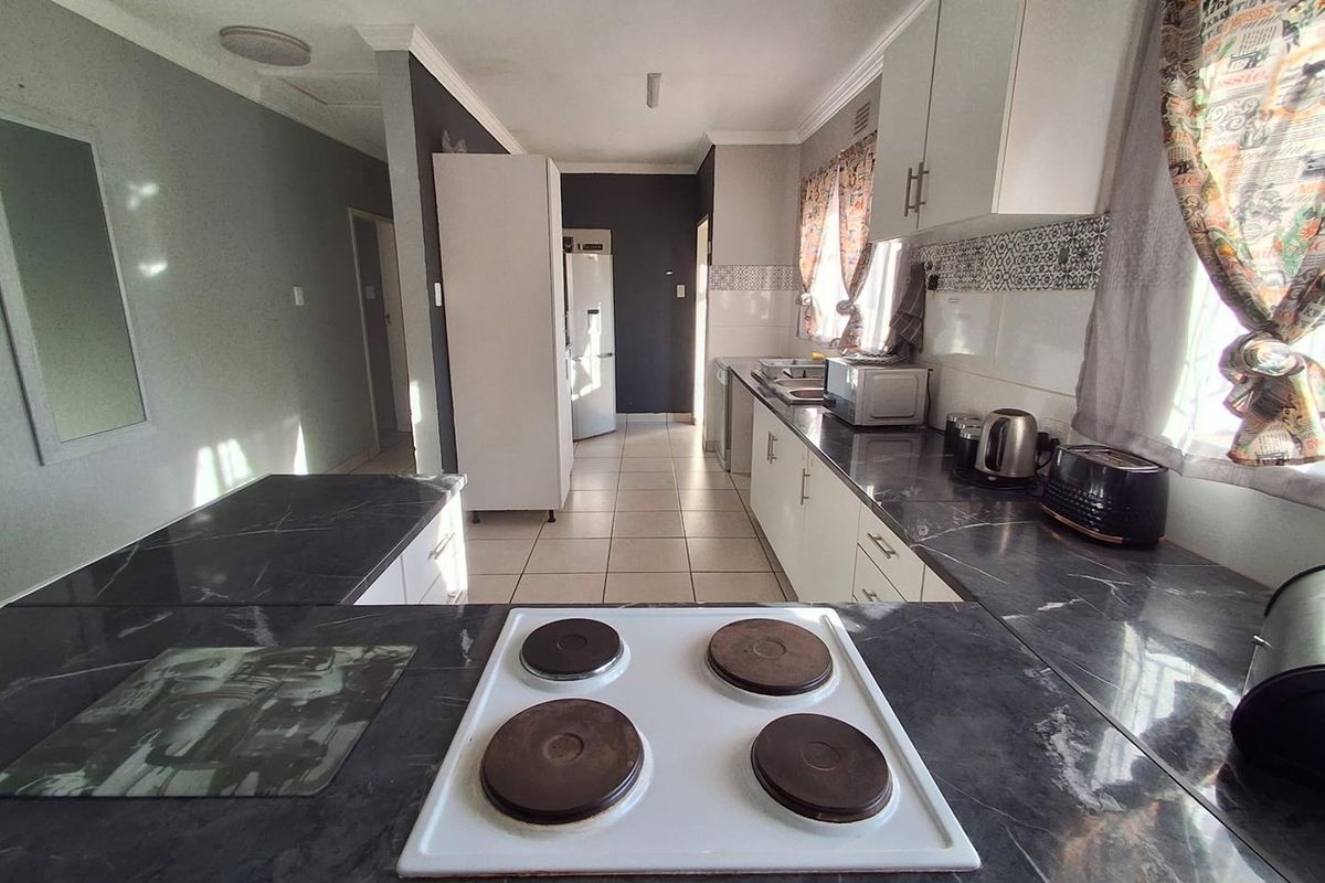 A functional kitchen featuring dark marble-effect countertops, white cabinetry, a four-plate electric hob, and tiled flooring with a neutral color palette.