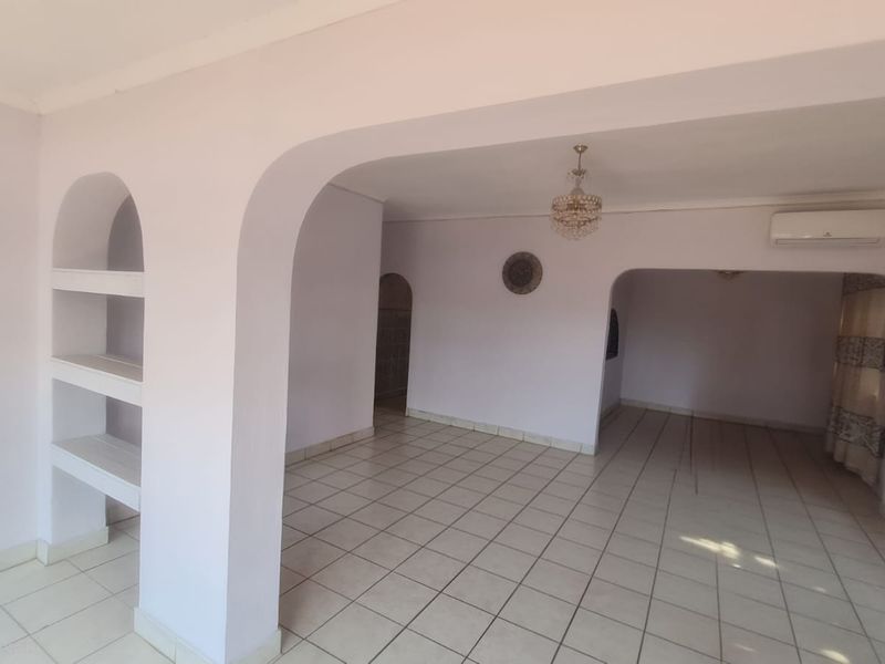 Spacious open-plan living area featuring tiled flooring, arched architectural details, built-in shelving, and a wall-mounted air conditioning unit.