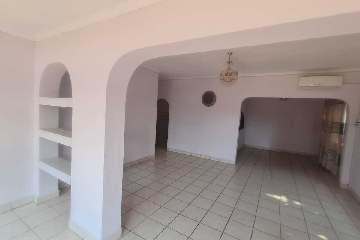 Spacious open-plan living area featuring tiled flooring, arched architectural details, built-in shelving, and a wall-mounted air conditioning unit.