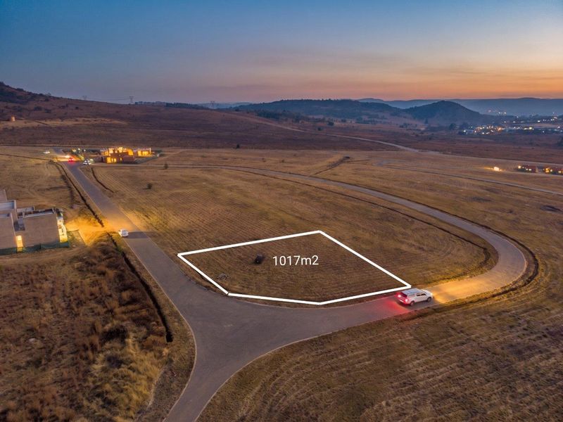 Aerial view of a 1017m2 vacant residential plot situated in a developed estate with paved road access and scenic landscape views.
