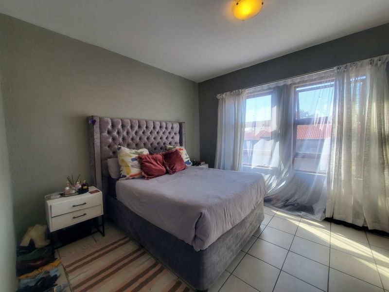 A bedroom featuring tiled flooring and large windows that allow for natural light, providing a functional space for rest.