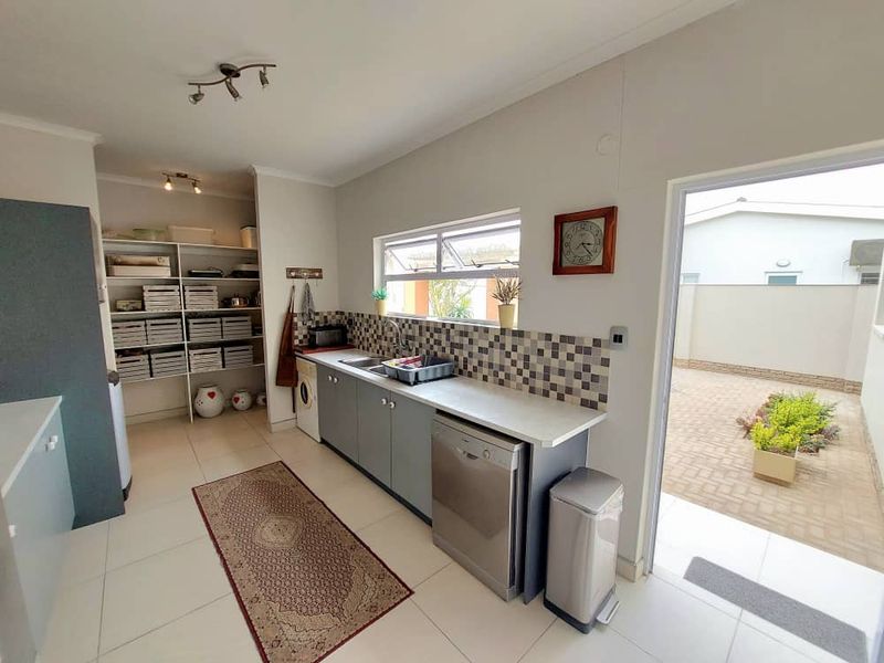A functional scullery area featuring built-in cabinetry, tiled splashback, stainless steel sink, and direct access to an outdoor paved courtyard.