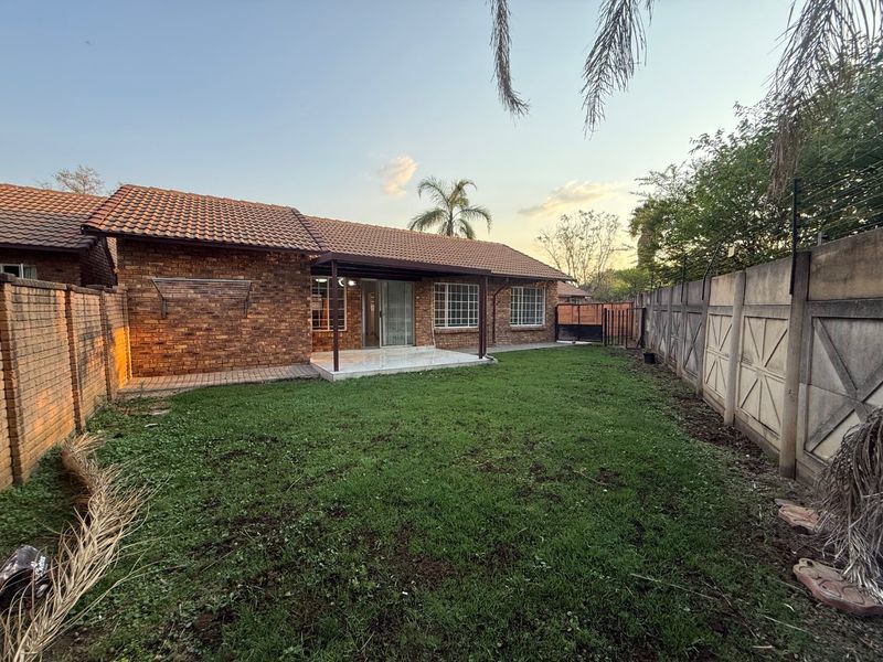 Rear view of the townhouse featuring a brick facade, tiled roof, covered patio area, and a private garden enclosed by precast boundary walls.