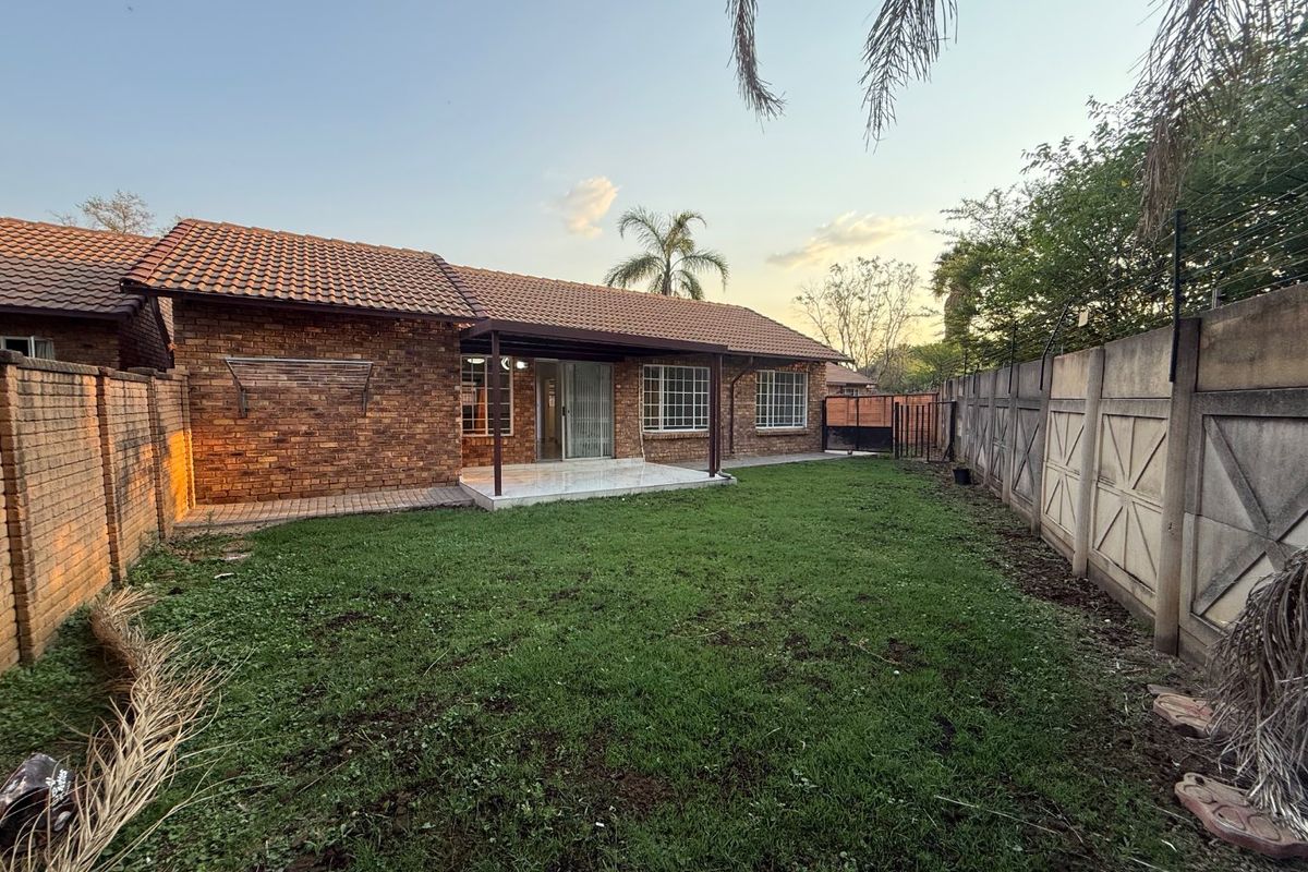 Rear view of the townhouse featuring a brick facade, tiled roof, covered patio area, and a private garden enclosed by precast boundary walls.