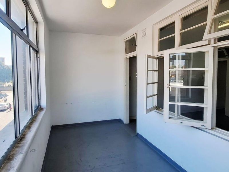 An enclosed balcony or sunroom featuring large windows, painted concrete flooring, and direct street views, offering a bright and versatile space.