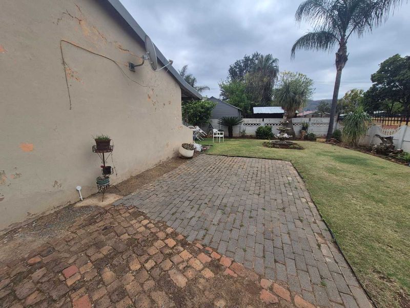 Rear garden area featuring a paved patio, lawn, and decorative fountain, with visible wear to the exterior wall finish.