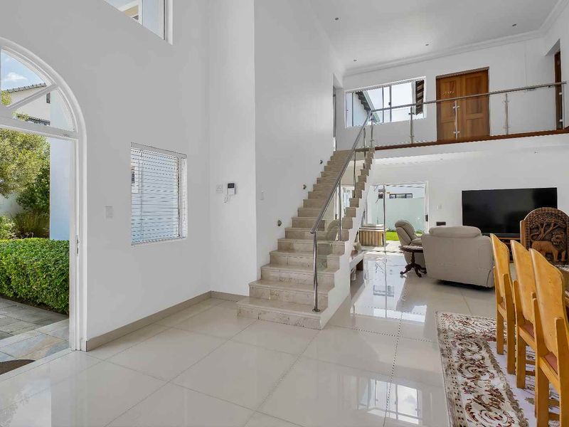Spacious open-plan living area featuring a grand staircase with glass balustrade, high ceilings, polished tile flooring, and direct access to the outdoor garden.