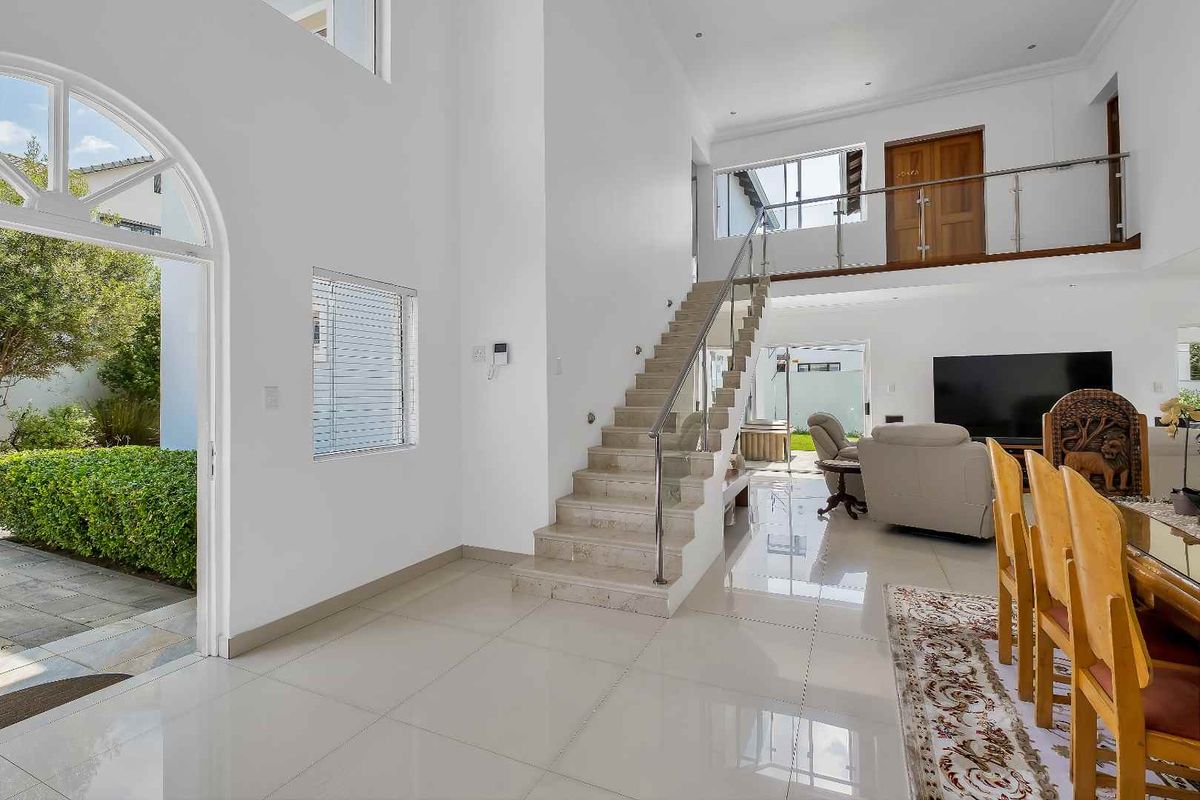 Spacious open-plan living area featuring a grand staircase with glass balustrade, high ceilings, polished tile flooring, and direct access to the outdoor garden.