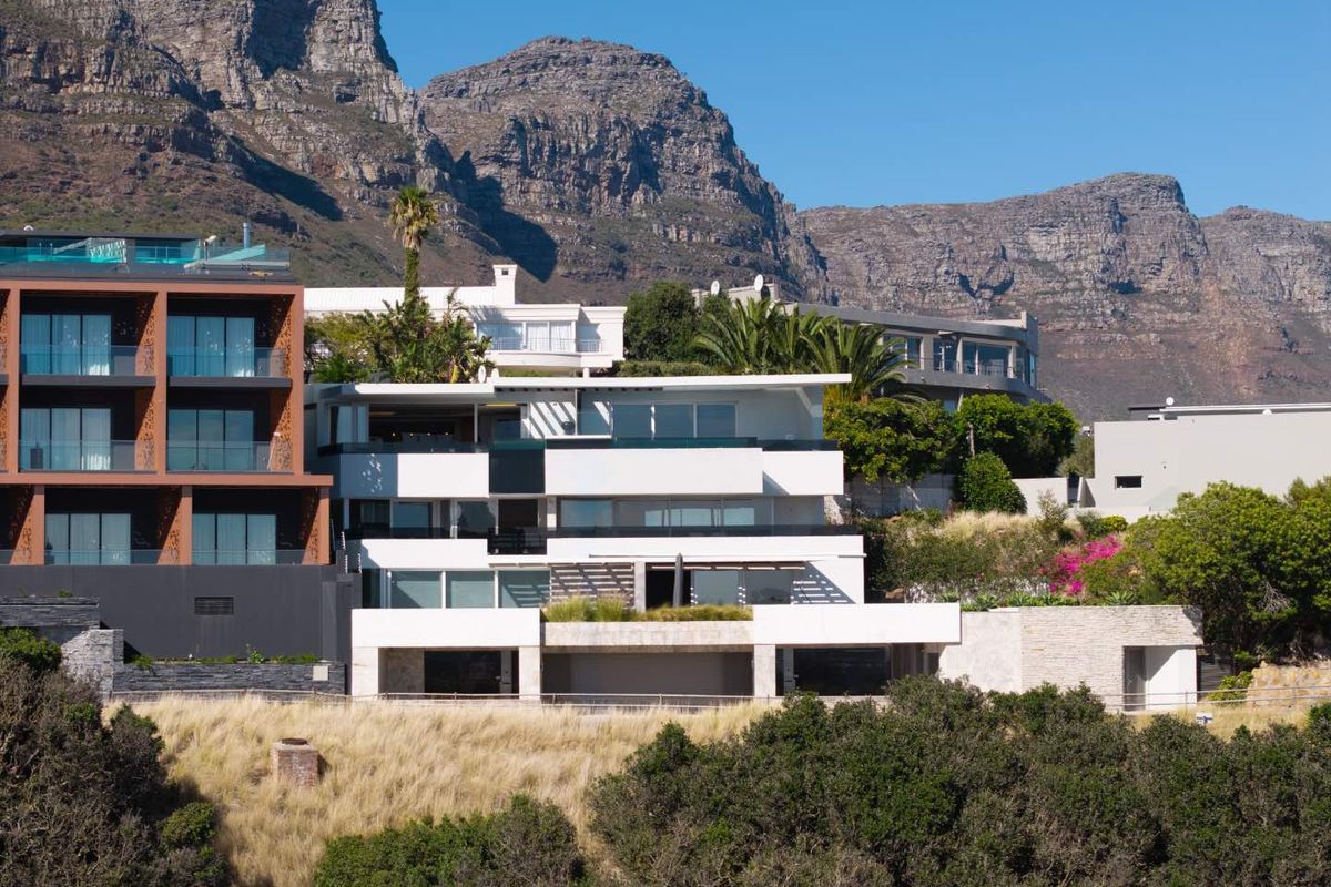 A modern multi-level apartment building featuring expansive terraces and stone facade elements, set against a dramatic mountain backdrop.