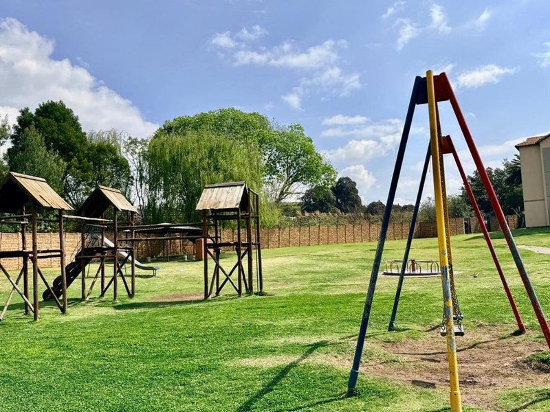 A communal garden area featuring a lawn and various fixed playground structures including swings and wooden play frames.